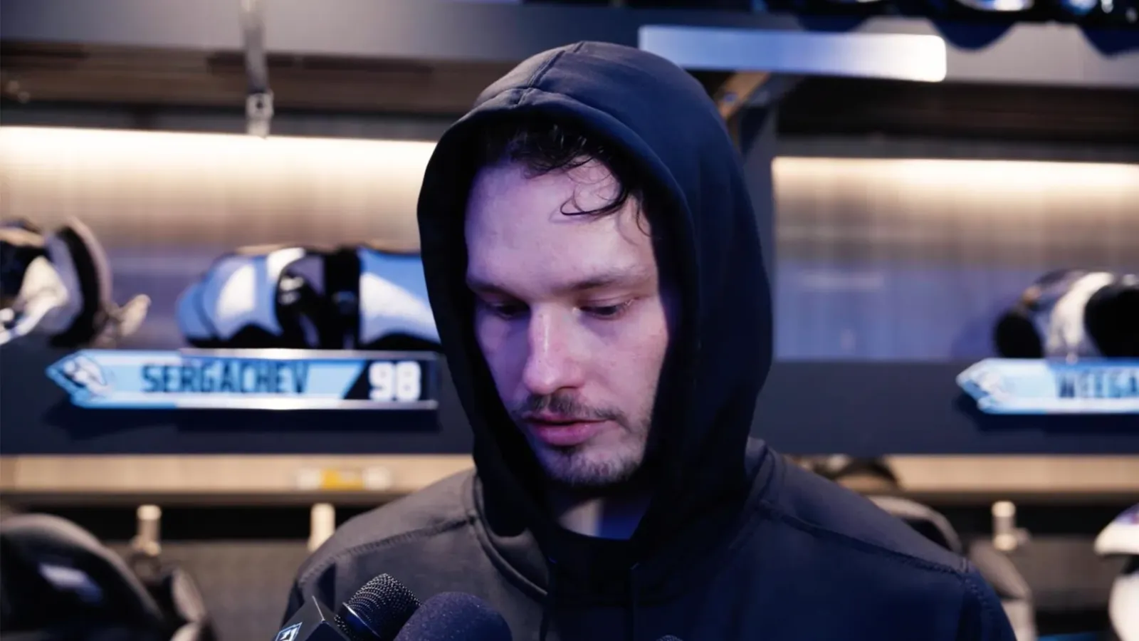 Mikhail Sergachev in a black hooded sweatshirt during his postgame interview in the Mammoth locker room, with his number 98 nameplate on the stall behind him